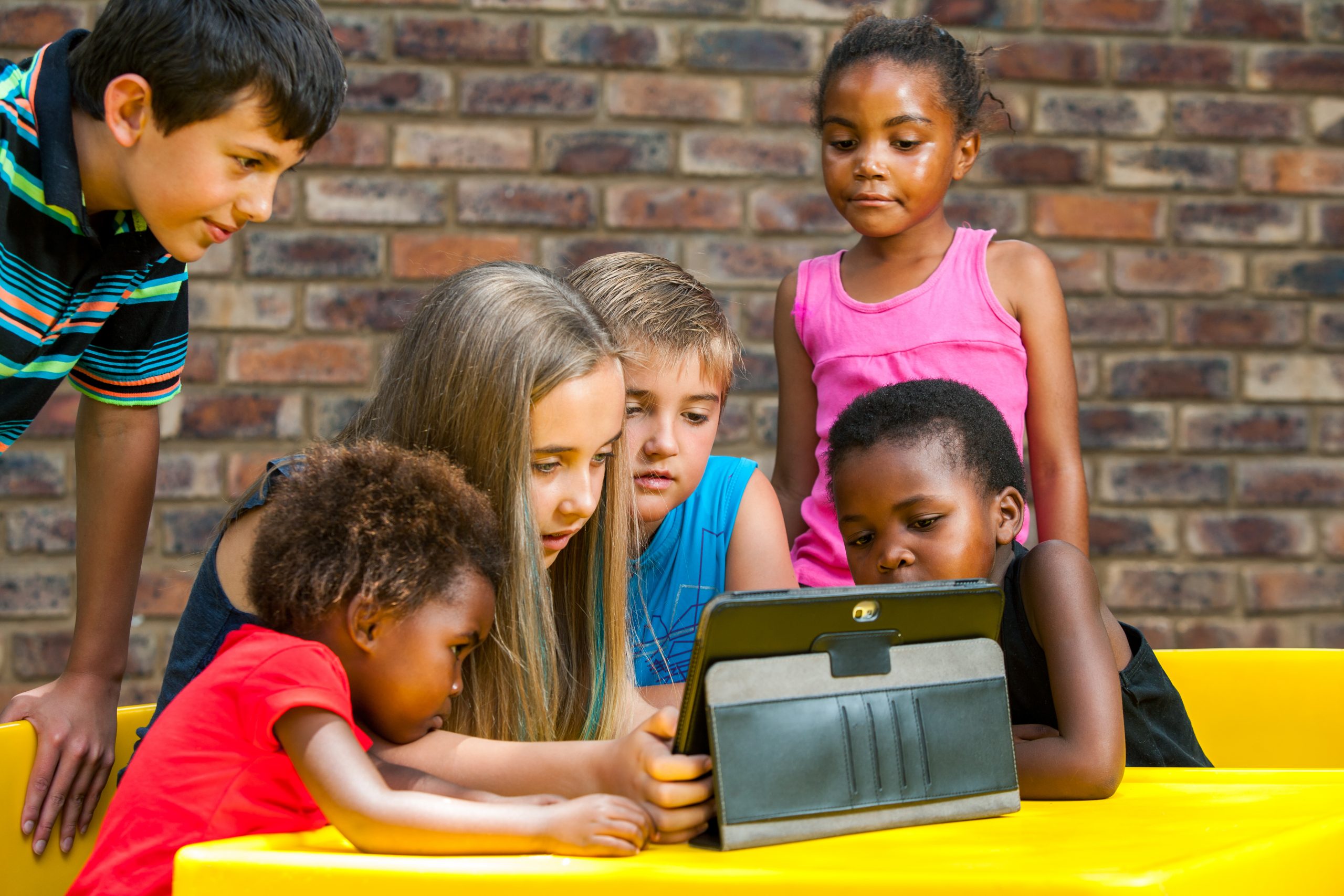 Bir çok ırktan bir grup çocuk açık havada tablete bakıyorlar.