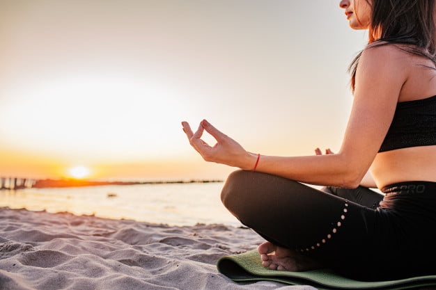 Plasebo kullanmak yerine sahilde kum ve güneş eşliğinde meditasyon yapan bir kadın.